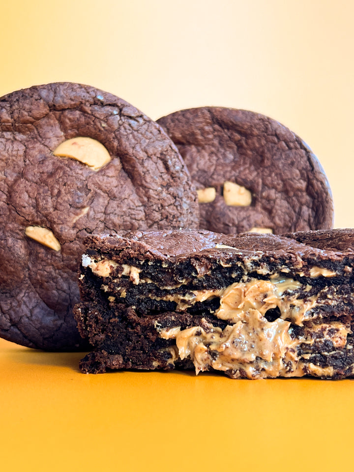 Two chocolate cookies with peanut butter chips behind a cut half, peanut butter filling showing