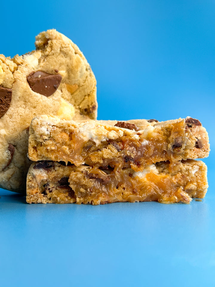 A stuffed cookie beside its two halves, caramel showing, on a blue background