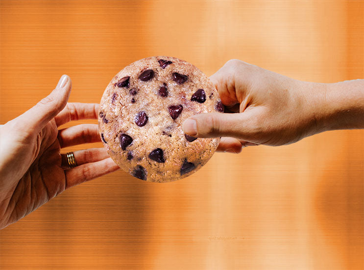 One hand passing a cookie to another against an orange wall