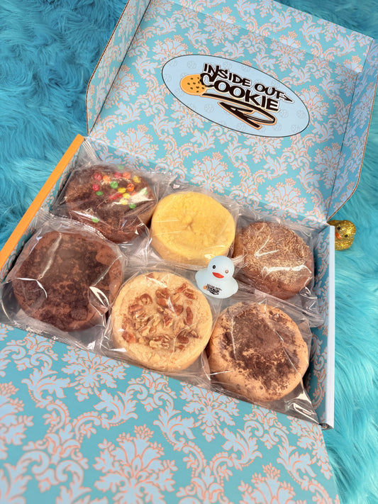 An open Inside Out Cookie mailer box holding six individually wrapped cookies, with the company logo printed inside the lid.