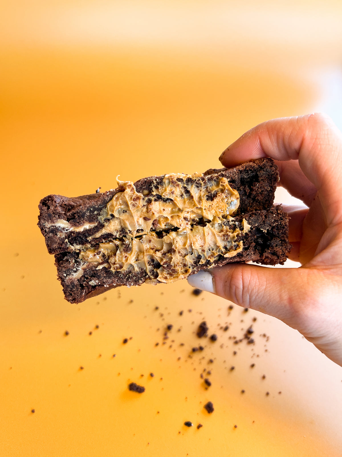 A chocolate peanut butter stuffed cookie pulled open in one hand, crumbs falling