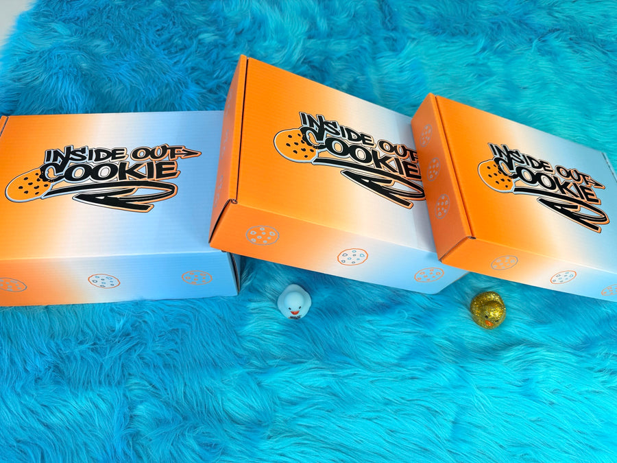Three Inside Out Cookie boxes and two rubber ducks on a blue rug