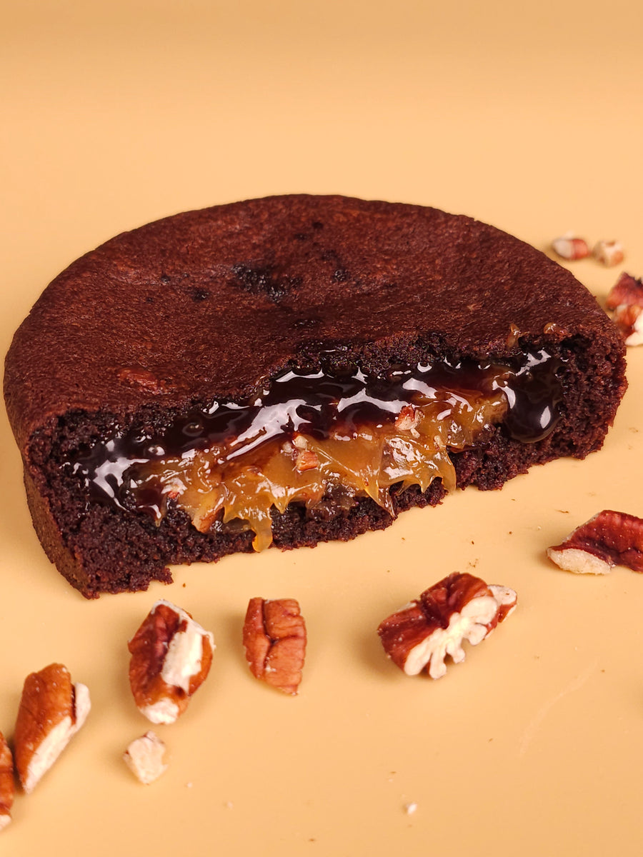A chocolate stuffed cookie cut open, caramel filling showing, pecan pieces scattered around it